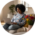 Mujer sonriente usando una laptop en el sofá, simbolizando la comodidad de la compra online.